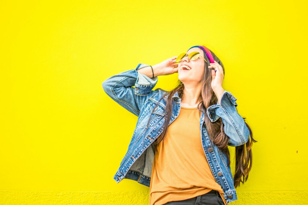 Une femme stylée en train de sourire devant un fond jaune fluo.