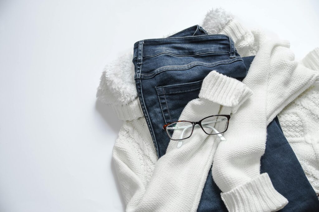 Jeans, lunettes et chandail de laine sur un fond blanc.