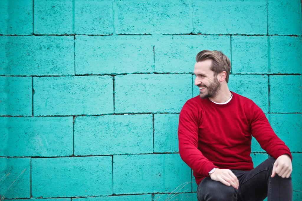 Homme heureux assis devant un mur de brique turquoise.